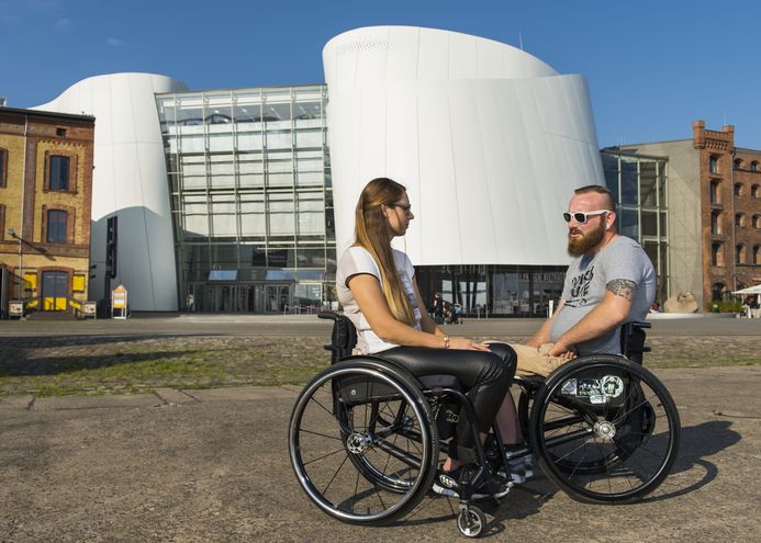 Eine Frau und ein Mann, beide in Rollstühlen, vor dem OZEANEUM Stralsund